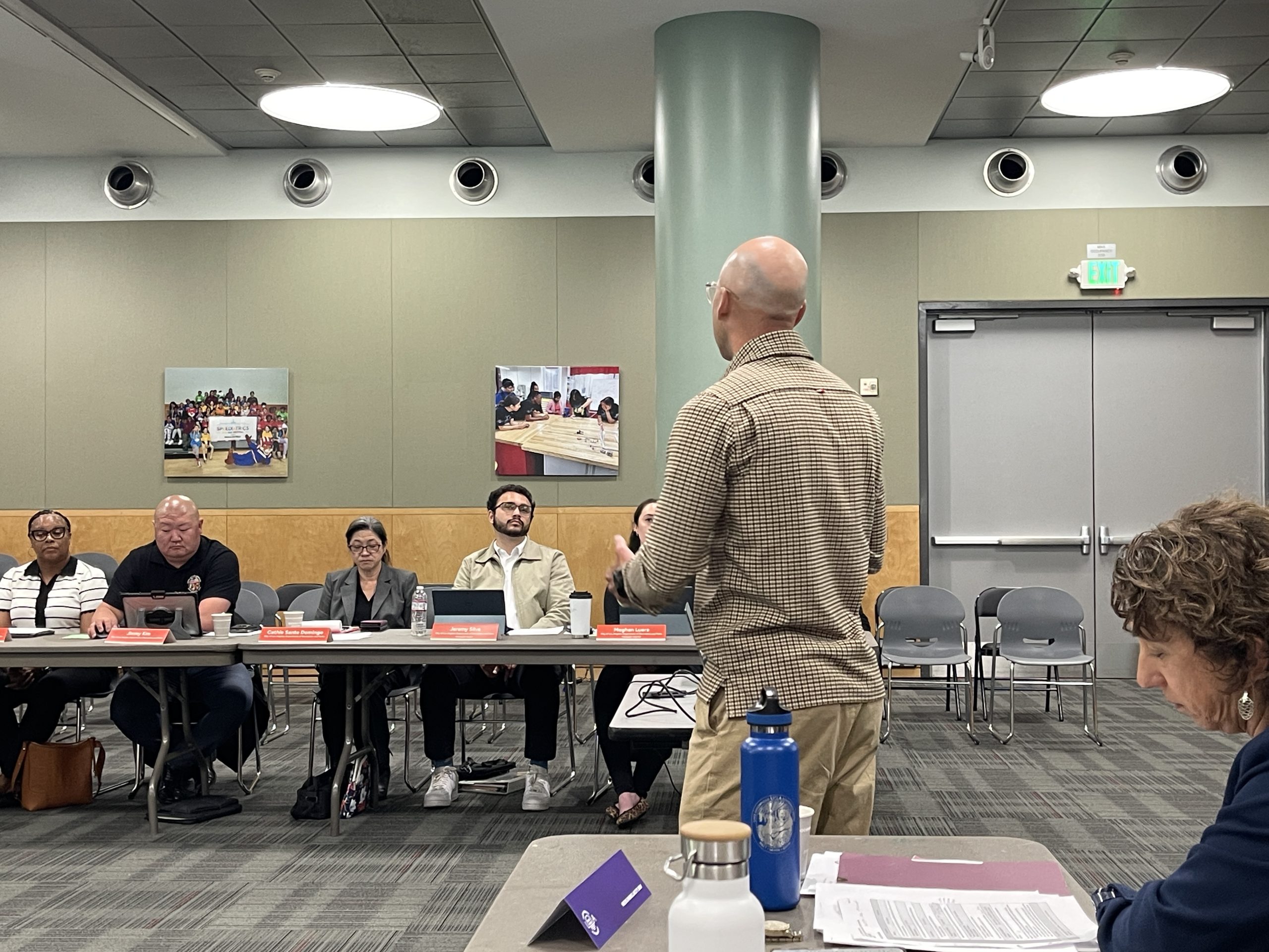 A man, seen from behind, is leading an engagement meeting with a group of people at a long conference table.