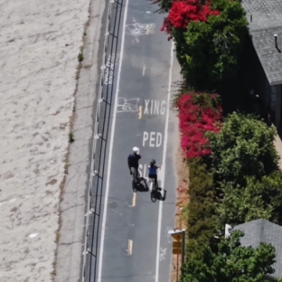 Aerial view of two people biking along a bike path. To the right is residential homes, and to the left is a concrete, channelized river.