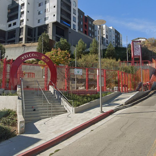 5-story building surrounded by red fencing with an arch that says "Welcome", greenery, and a clear blue sky.