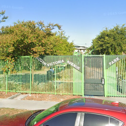 Red sedan parked in front of light green gate and fence with a sign that says "South Victoria Avenue Park."
