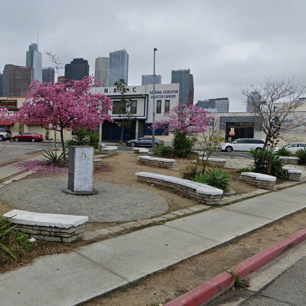 Small. urban park with white-top seating areas and pink flowering trees on an overcast, cloudy day.